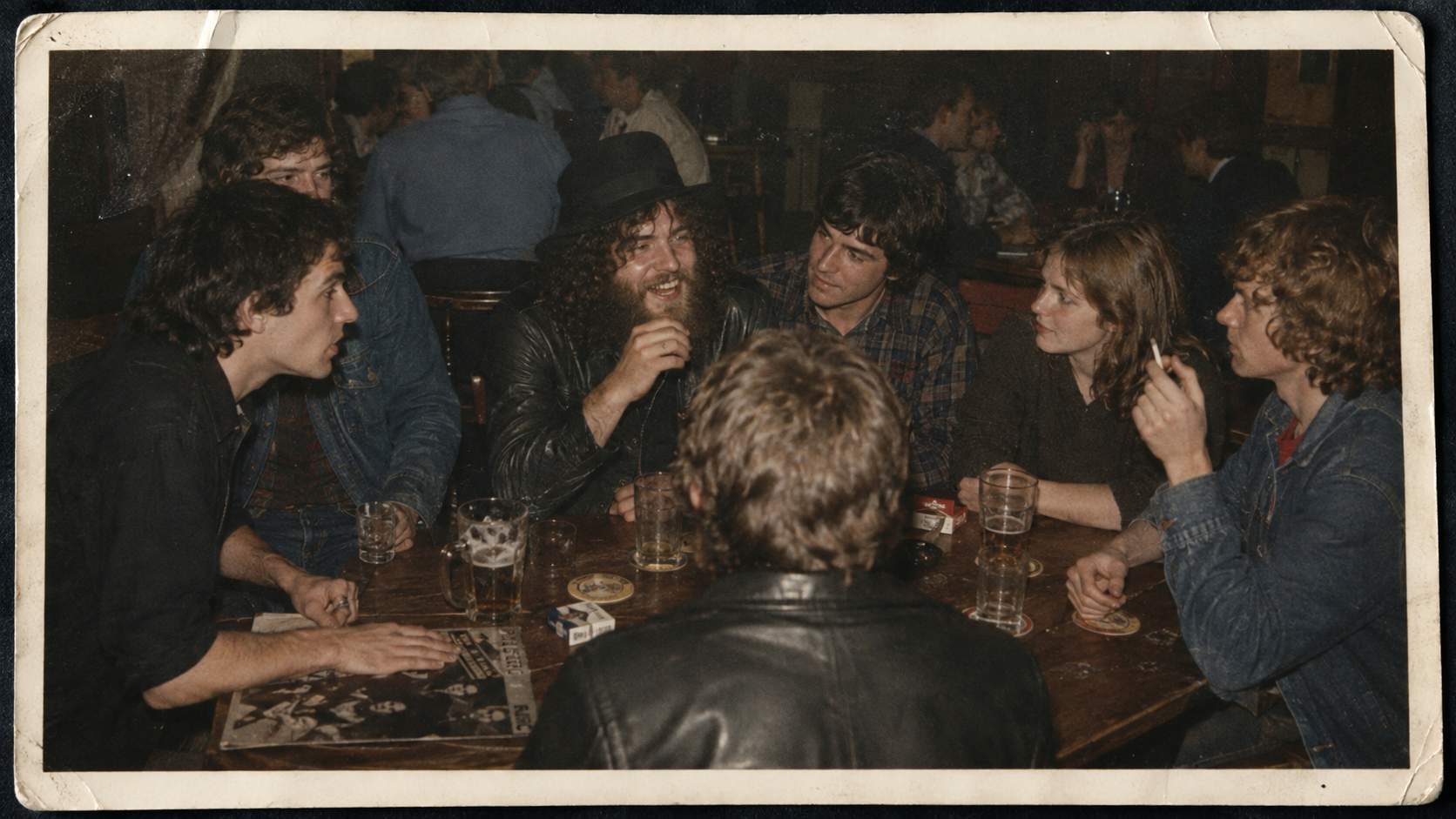 An old colour photograph of young people round a pub table with beer glasses and cigarettes.